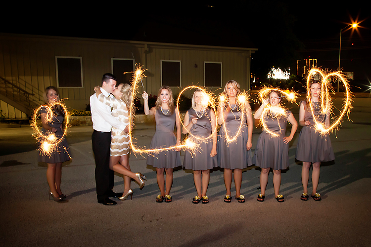 Bridesmaids doing a sparkler love while bride and grrom embrace.