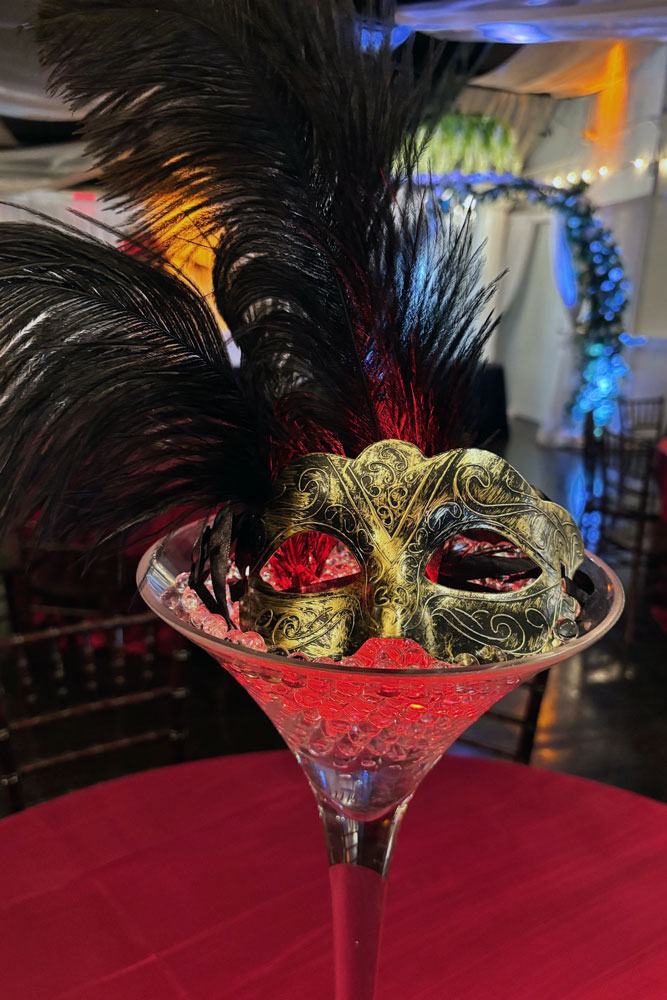 themed masquerade ball centerpiece in a glass vase with accent lighting