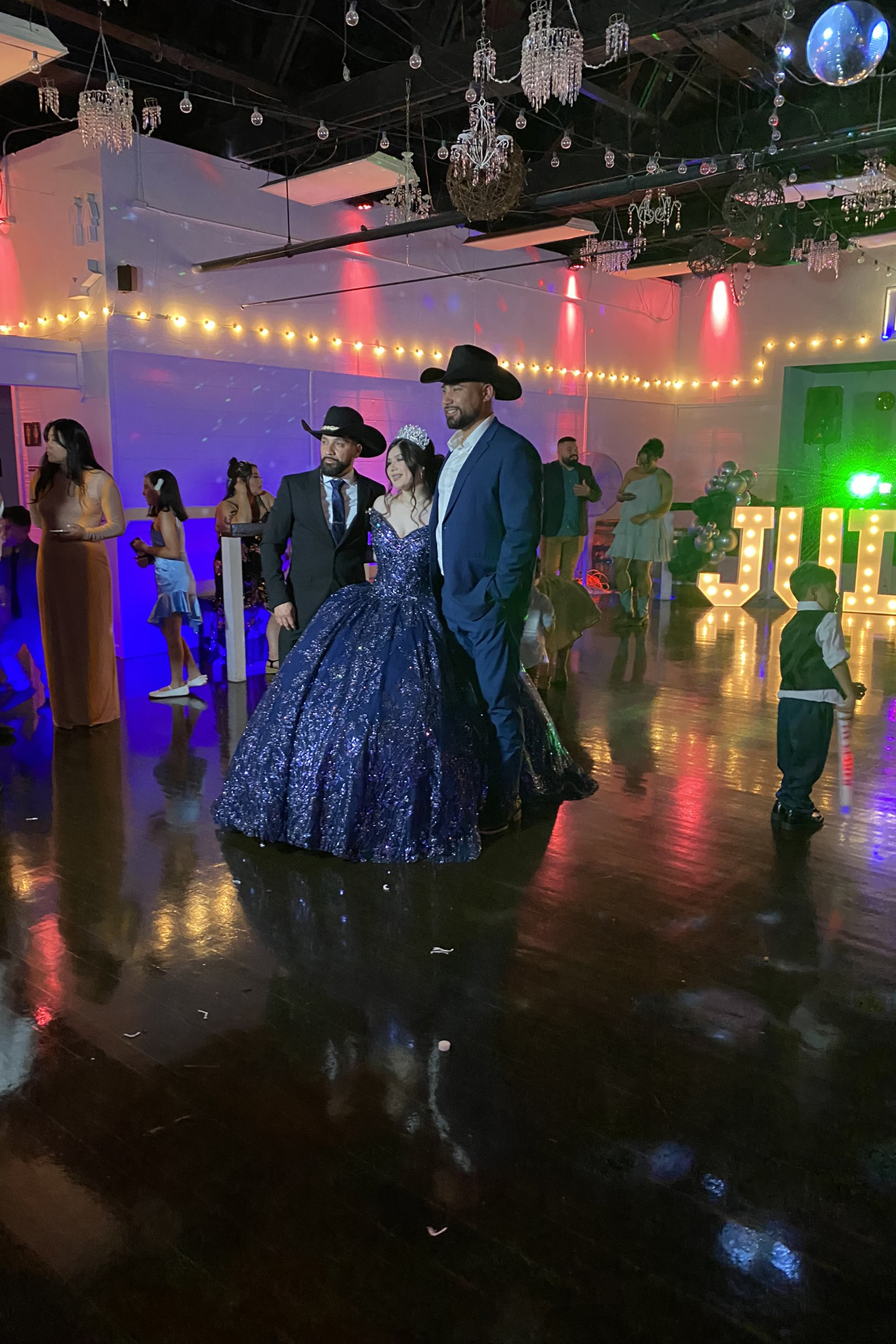 Two proud fathers posiing with the quince girl of honor oon dance floor in a throne chair.