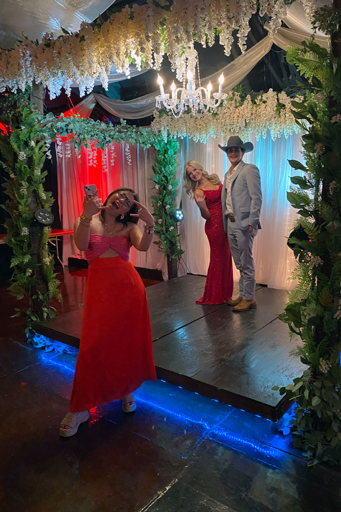 Bride and groom on greenery and floral gazebo posing for a guest.