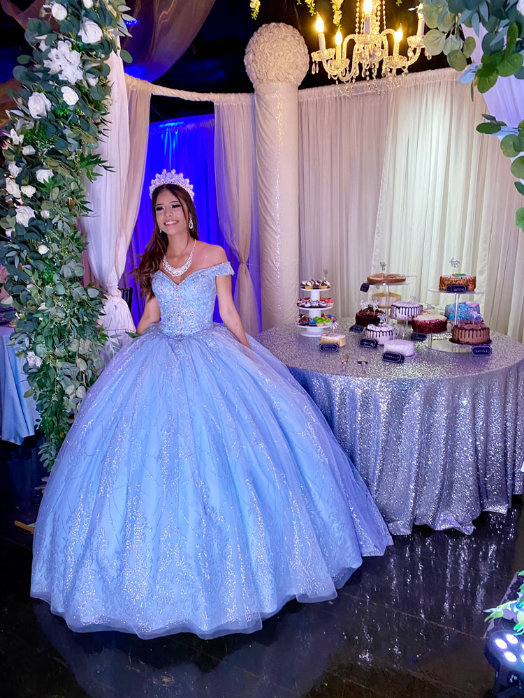 Quince girl sharing a memorable moment by her cake table under soft blue reception lighting